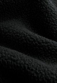 Schwarzer Fleece-Stoff mit einer weichen, strukturierten Oberfläche, die Wellen und Falten zeigt. Das Material ist leicht und warm, geeignet für Kleidung.