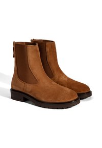 Bottines en suede marron avec des panneaux élastiques sur les côtés, orteils ronds et un petit talon carré. Présente des coutures visibles et une languette pour un enfilage facile.