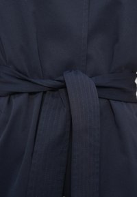 Μπουφάν σε ναυτικό μπλε χρώμα από απαλό ύφασμα, με δεμένη ζώνη και κάθετες λεπτές ρίγες στη ζώνη. Το σχέδιο περιλαμβάνει καθαρές ραφές και δομημένη εφαρμογή.