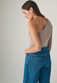 Brauner einseitiger Bodysuit aus dehnbarem Material, kombiniert mit hochgeschnittenen blauen Denim-Jeans mit Gesäßtaschen und einer lockeren Passform.