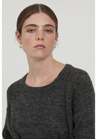 Maglione grigio lavorato a maglia con scollo rotondo e maniche raglan. La texture appare morbida, con un motivo sottile e ruvido su tutta la superficie.