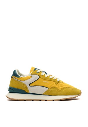 Gul og beige sneaker med grønne accenter, hvide snørebånd og beige sål, mærket "HOFF" på siden og på hælen, set fra siden mod hvid baggrund.
