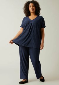 Navy loungewear sæt, der inkluderer en kortærmet V-hals top med et struktureret diamantmønster og løstsiddende bukser, begge lavet af blødt stof.