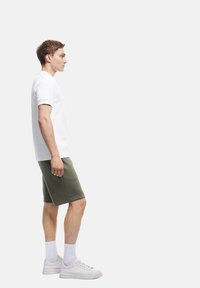 Biała koszulka z okrągłym dekoltem, oliwkowe szorty, białe trampki, białe skarpetki sięgające kostek. Swobodny styl sportowy, płaski design, gładka tekstura.