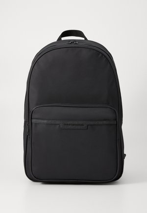 Sac à dos en nylon noir avec une forme arrondie, poche avant zippée et plaque de logo. Texture lisse avec des bretelles rembourrées.
