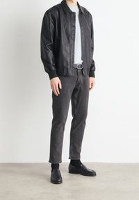 Musta nahkainen lentäjän takki resorireunuksilla, vaaleanharmaa t-paita, tummanharmaat slim-fit-farkut ja mustat loafersit koristetikkauksilla.