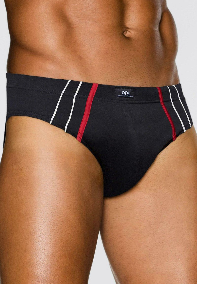 Torso maschile in forma che indossa slip neri con strisce verticali rosse e bianche e logo bpc sulla cintura, su sfondo neutro.