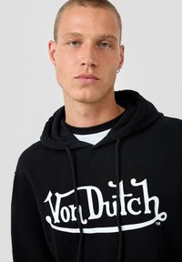 Zwarte hoodie met een wit 'Von Dutch' logo, trekkoordkap, en een gelaagd uiterlijk met een zwart-wit gestreepte shirt eronder.