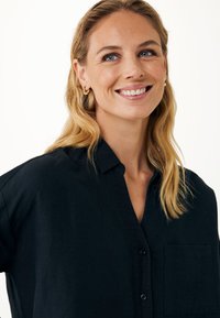 Czarna koszula zapinana na guziki z kieszenią, wykonana z teksturowanej tkaniny; posiada kołnierzyk i luźny krój.