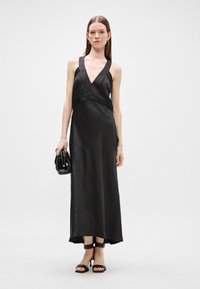 Čierne saténové maxi šaty s hlbokým V výstrihom, priliehavým korzetom a splývavou sukňou. Kombinované s čiernou kabelkou a remienkovými sandálmi.