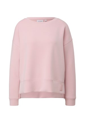Sweat-shirt rose clair à manches longues, col rond, épaules tombantes et petit patch logo rectangulaire près de l’ourlet côté gauche.