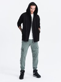 Zwarte rits hoodie met een grote capuchon, gecombineerd met lichtgroene cargobroeken met meerdere zakken en zwarte sportschoenen.