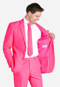 Completo rosa brillante con cravatta e camicia abbinate. Tessuto con texture, design aderente e tasca interna etichettata "Opposuits." Bottoni sulla giacca visibili.