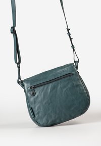 Borsa a tracolla in pelle verde acqua con forma curvilinea, dotata di tasca frontale con zip e tracolla regolabile. Texture liscia, dettagli di cucitura discreti.