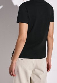 Svart t-shirt med kort ärm, tillverkad av bomull, med en figurnära passform och en slät yta. Bärs tillsammans med ljusbeiga byxor, som visar en avslappnad stil.