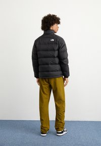 Chaqueta acolchada negra con textura de rombos, cuello alto y logo blanco. Combinada con pantalones verde oliva y calzado en blanco y negro.