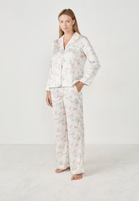 Conjunto de pijama de satén con una base rosa clara y patrones de flores y cintas en azul y rosa. Manga larga, parte superior con botones y pantalones de corte holgado.