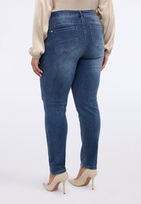 Wąskie jeansy z ciemnoniebieskiego denimu o wysokim stanie, posiadające dwie tylne kieszenie i gładką, lekko wyblakłą fakturę. Połączone z beżowymi szpilkami.