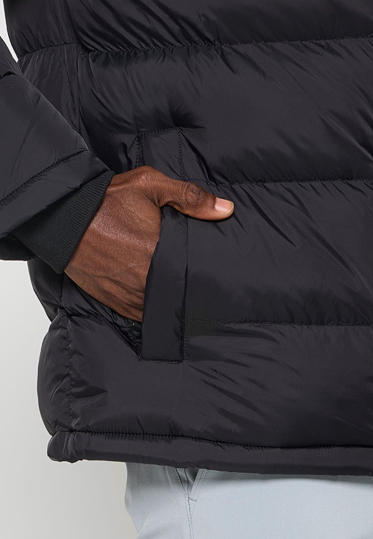Schwarze Steppjacke mit quilteter Textur, ausgestattet mit einer Seitentasche und gestrickt Manschette am Handgelenk. Leichtes Design, wasserabweisendes Material.