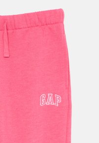Ružové bavlnené jogger nohavice s elastickým pásom, bočnými vreckami a bielym vyšitým logom "GAP" na ľavom stehne.