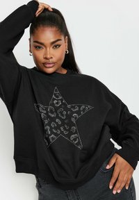 Svart sweatshirt med lös passform, prydd med en stor stjärndesign i silverfärgad djurtrycksstuds. Ribbad mudd och nederkant.