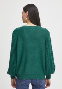 Pull en tricot vert avec une coupe décontractée, doté de manches texturées et d'un ourlet côtelé. Idéal pour superposer par temps frais.