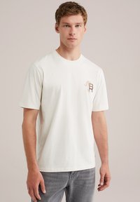 White cotton t-shirt featuring a small embroidered logo on the chest. Short sleeves and crew neck design. Textured fabric.