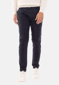Pantaloni chino in cotone blu scuro, slim fit con una leggera lucentezza, dotati di chiusura con bottone frontale, tasche laterali e lacci bianchi sulle sneakers.