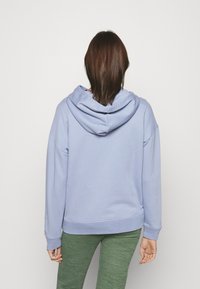 Sudadera con capucha de color azul claro, con un bolsillo canguro en la parte frontal y cordones en la capucha, combinada con pantalones verdes texturizados. Tejido suave de mezcla de algodón.