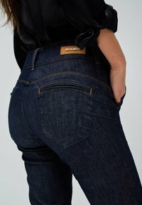 Jeans de mezclilla azul oscuro con corte slim, que cuentan con un parche de cuero en la parte trasera de la cintura, costuras en contraste y dos bolsillos traseros.