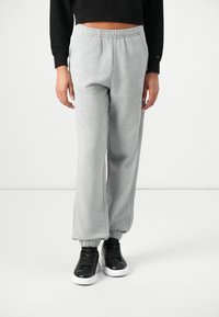 Lichtgrijze sweatpants van zacht materiaal, met een elastische tailleband en opgerolde enkels, gedragen met zwarte sneakers.