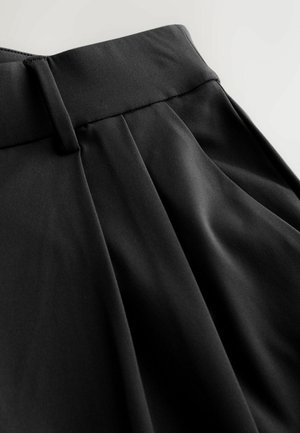 Mustad püksid, millel on sile ja kerge tekstuur, kohandatud vöökoht ja volditud esikülg, rõhutades struktureeritud siluetti.