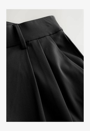 Juodos kelnės su lygiu, lengvu audiniu, turinčios priderintą juosmenį ir priekyje klostėmis papuoštą dizainą, pabrėžiančios struktūruotą siluetą.