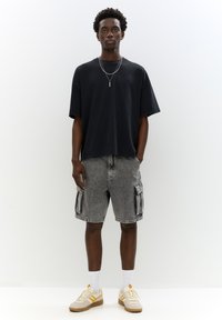 T-shirt en coton noir, coupe décontractée, associé à un short cargo gris avec des poches latérales. Des baskets crème et jaunes complètent le look.