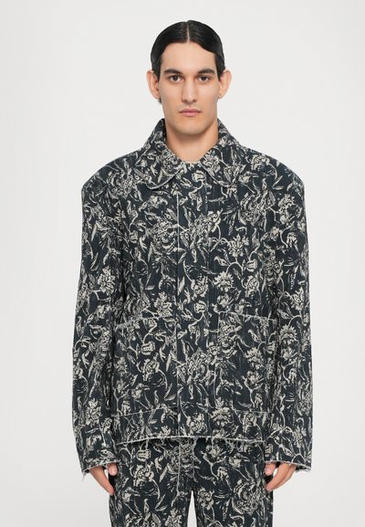 Veste en denim noire avec un motif floral blanc. Comprend un grand col et des coutures visibles. Poches à l'avant avec une forme carrée.