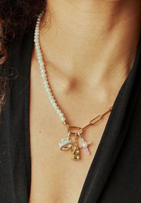 Collier en perles avec quincaillerie dorée, comportant trois pendentifs : une couronne, un ours et une croix rose, chacun avec des textures et des couleurs distinctes.
