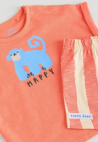 Korallenfarbiges Shirt mit einem blauen Affen-Graphic und dem Text "HAPPY". Passende Shorts mit abwechselnden korallenfarbenen und cremefarbenen Streifen. Weicher Stoff, lässiger Stil.