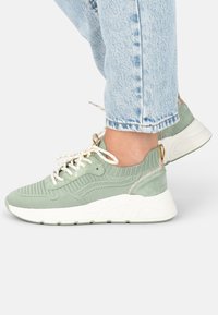 Light green sneakers featuring a textured fabric upper, white sole, and gold accents, with contrast laces and a cushioned design.