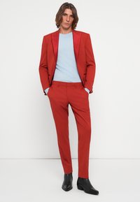Rød dressjakke med matchende bukser, lett stoff, slank design, parret med en lyseblå genser og svarte dressboots.