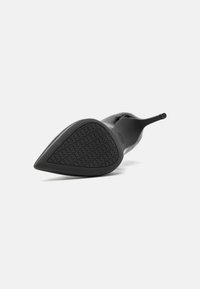 Chaussure à talon haut en cuir noir avec un bout pointu et une semelle en caoutchouc texturé présentant un motif géométrique. Design épuré avec une silhouette courbée.