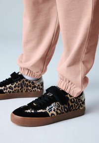 Mustad ja leopardimustriga tossud takjakinnituse ja kummist tallaga, kombineeritud mansetiga roosade dressipükstega. Tekstuurne pealispind ja kontrastsed detailid.