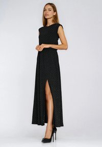 Czarna maxi sukienka w grochy z bocznym rozcięciem, krótkimi rękawami typu cap i zwiewną tkaniną. Noszona z czarnymi butami na wysokim obcasie.