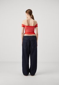 Top a righe rosse, senza spalle, abbinato a jeans in denim scuro e larghi. Il top presenta maniche corte e una vita aderente.