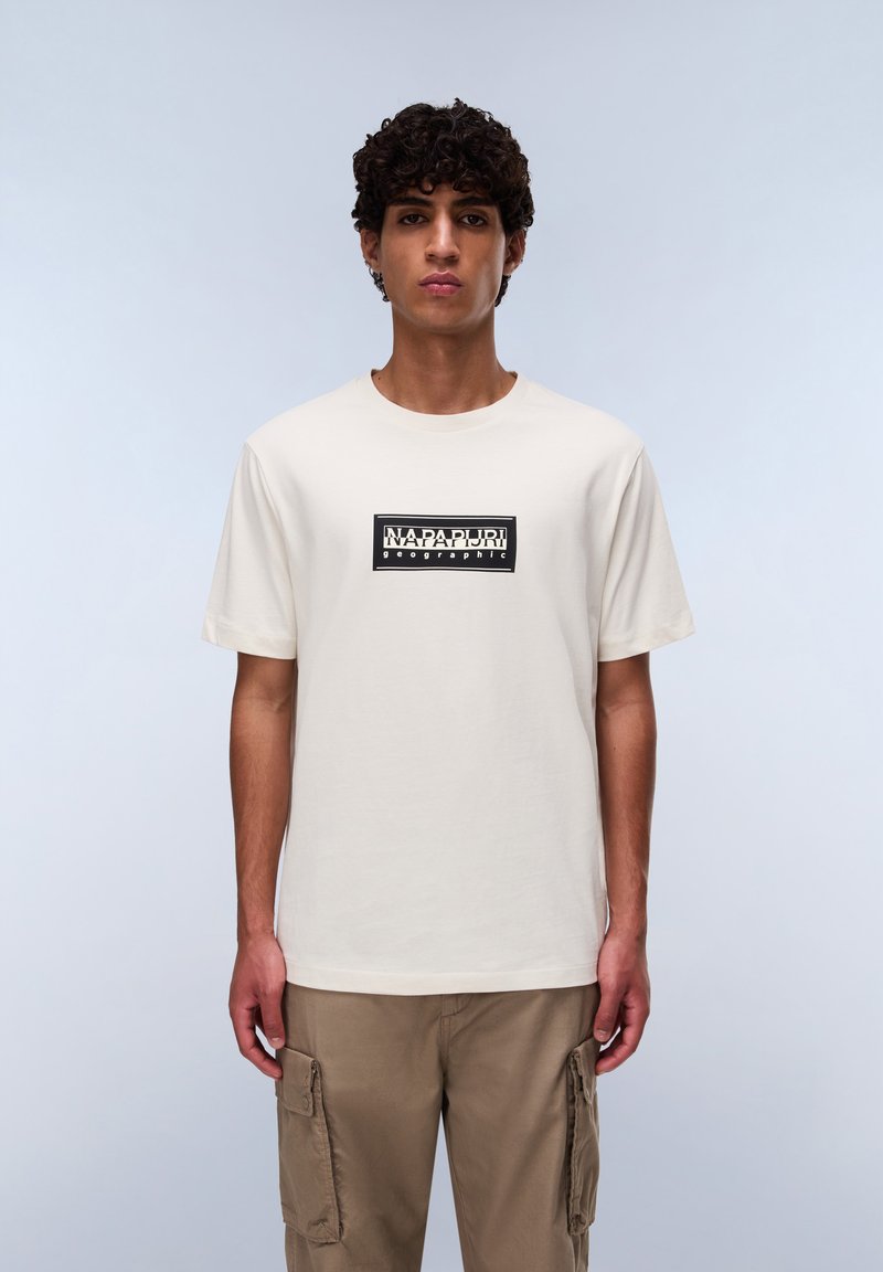 Beige bomulds t-shirt med korte ærmer, med et rektangulært sort logo med hvid tekst i midten. Casual pasform, enkelt design.
