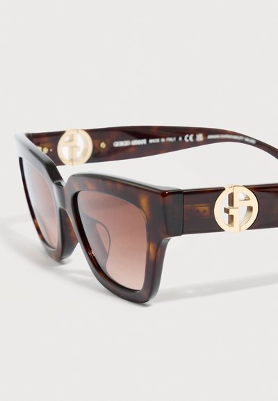 Καφέ ορθογώνια γυαλιά ηλίου από χελώνα με φακούς διαβάθμισης και χρυσές κυκλικές διακοσμήσεις με λογότυπο στα μπράτσα των κρικελιών.