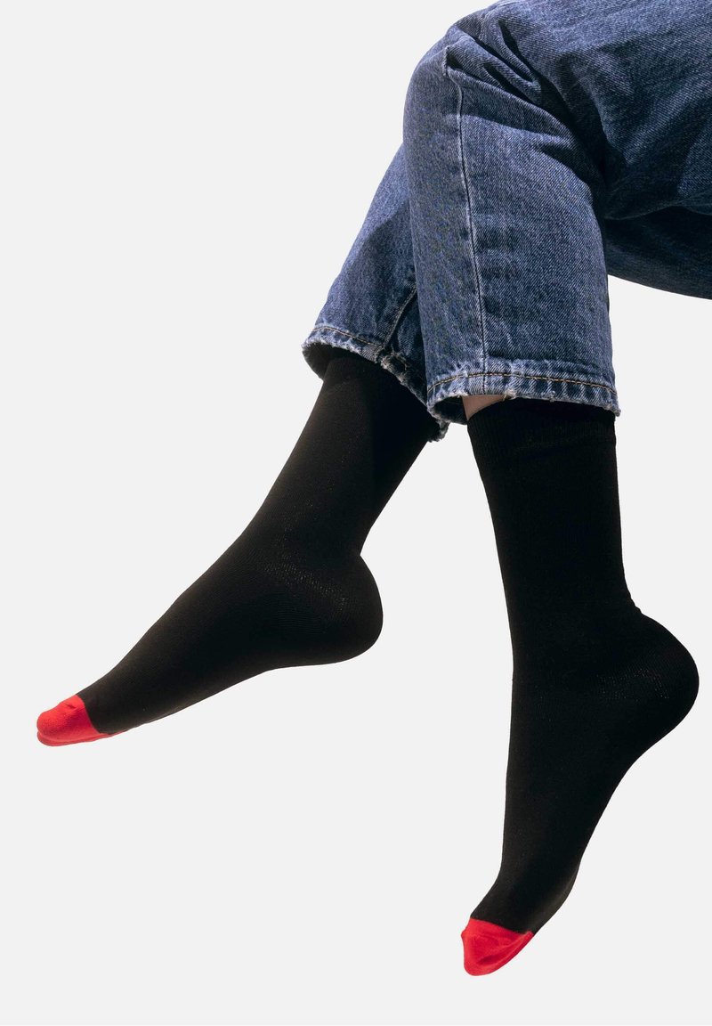 Czarne skarpetki z czerwonymi akcentami na palcach noszone z podwiniętymi niebieskimi dżinsami. Tkanina wydaje się gładka z delikatnym połyskiem.