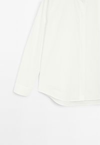 Camicia bianca a maniche lunghe con colletto, orlo dritto e polsini con bottoni, caratterizzata da una consistenza morbida e leggera del tessuto.