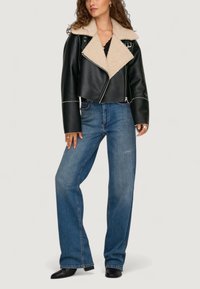 Schwarze Leder-Cropped-Jacke mit hellem Shearling-Kragen, kombiniert mit hellblauen Schlagjeans und schwarzen Knöchelstiefeln.