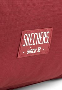 Bolsa de tela roja con un destacado parche del logo blanco "SKECHERS" con el texto "desde 92" bordado en el lateral en un diseño rectangular.