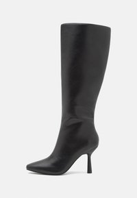 Botte en cuir noire montant jusqu'au genou, avec bout pointu et talon haut fin, sur fond blanc.